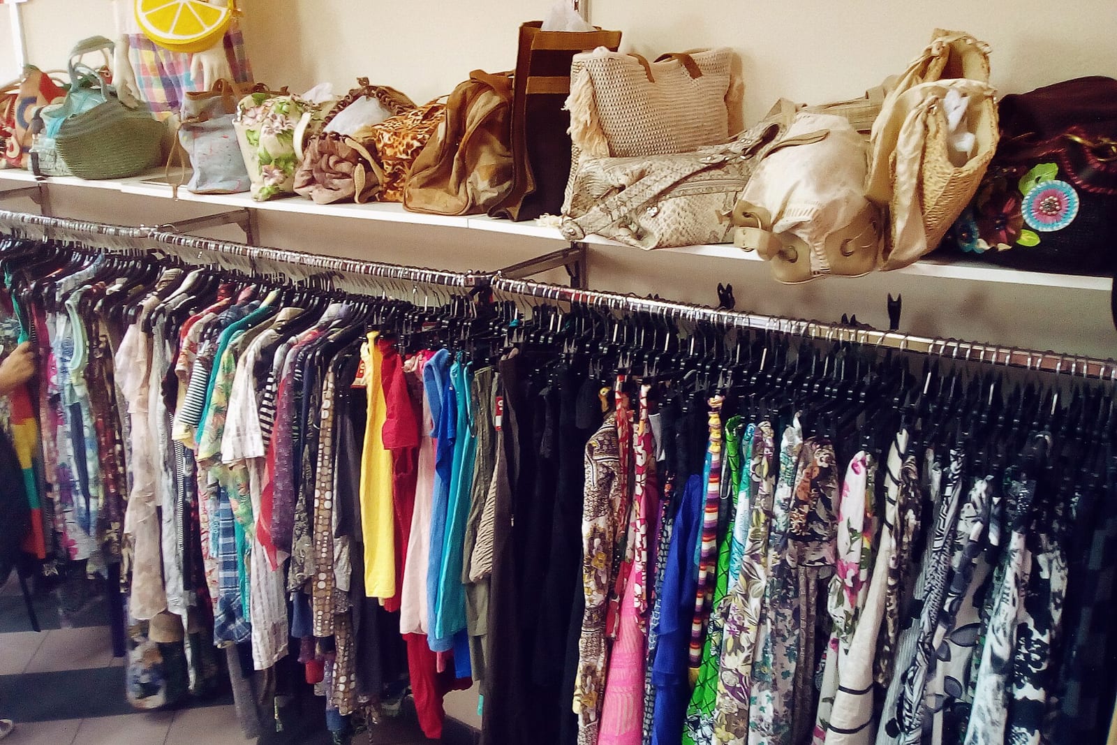 Racks of colorful secondhand clothes under shelves of bags